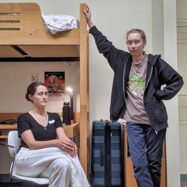 a mother and daughter lean up against a wooden bunk bed in a college dormitory